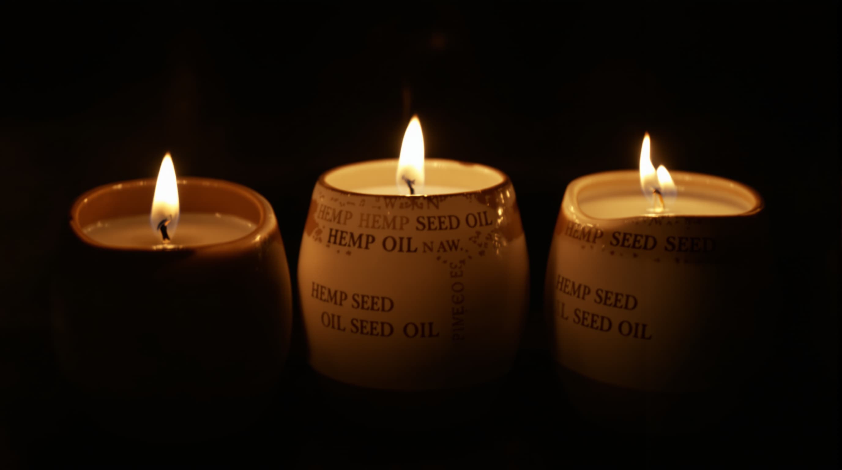 Three lit hemp seed oil candles in ceramic vessels in a dark room