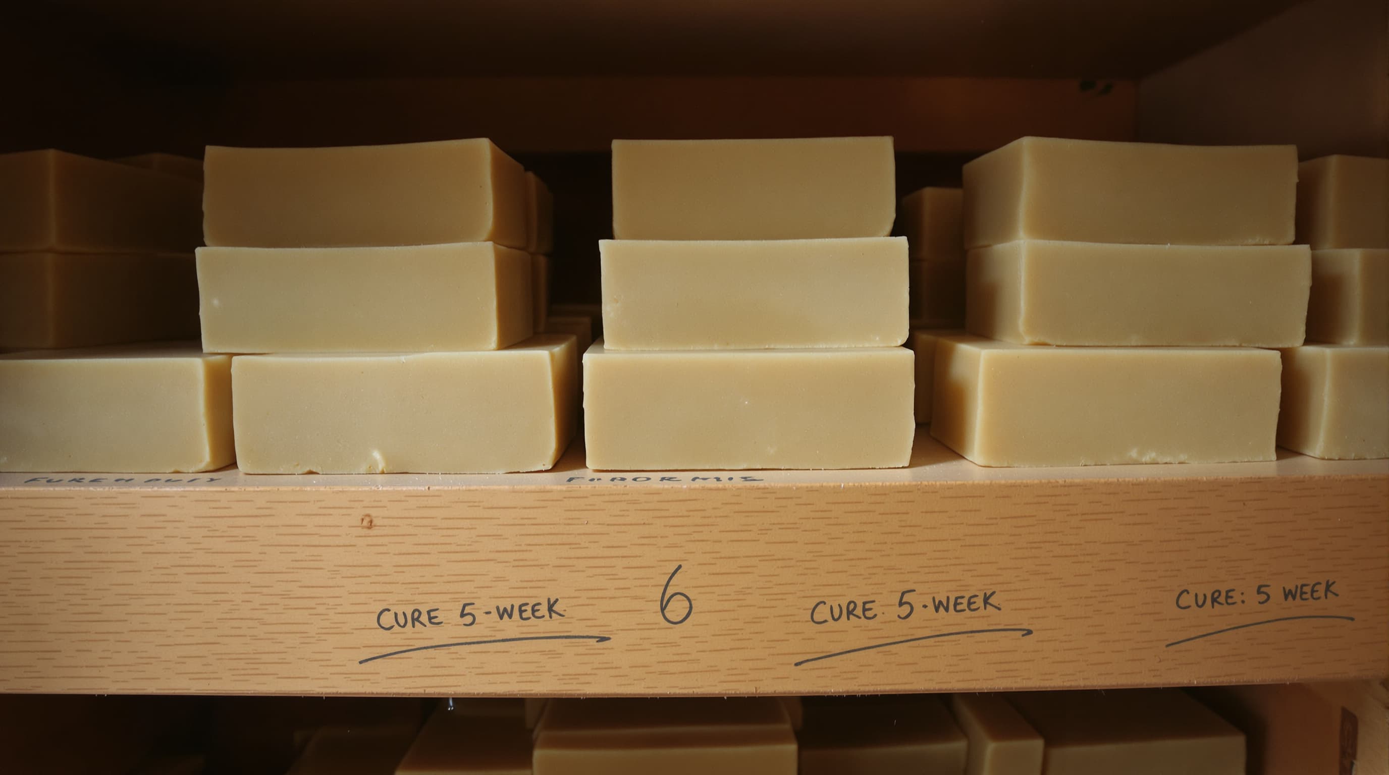 Curing hemp soap bars on a wooden shelf with cure dates penciled on the wood
